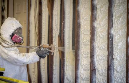 Picture of a person doing spray foam insulation. You can see the person is wearing spray foam insulation kit with spray foam insulation machine.