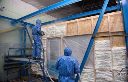 Picture of two persons doing spray foam insulation. You can see the two people are working with full spray foam insulation equipment