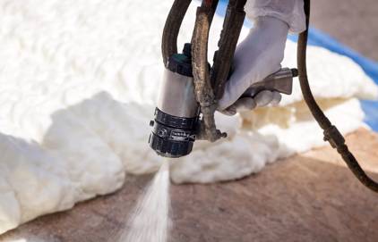 Picture of spray foam insulation contractor, spraying insulation. You can see white insulation spraying on surface.